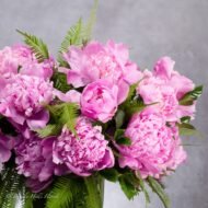 Elegant pink peony arrangement in a clear 12-inch glass vase with umbrella ferns and Gardenia foliage.